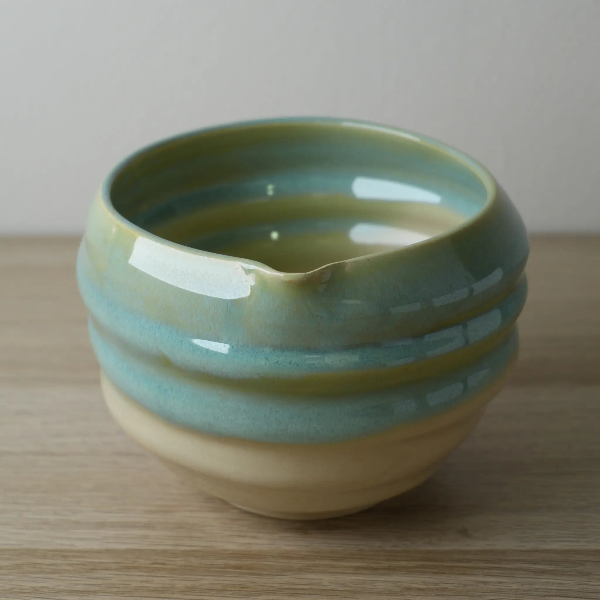 Cuenco de cerámica con borde azul verdoso y base beige del Set Cerámica Sora sobre mesa de madera