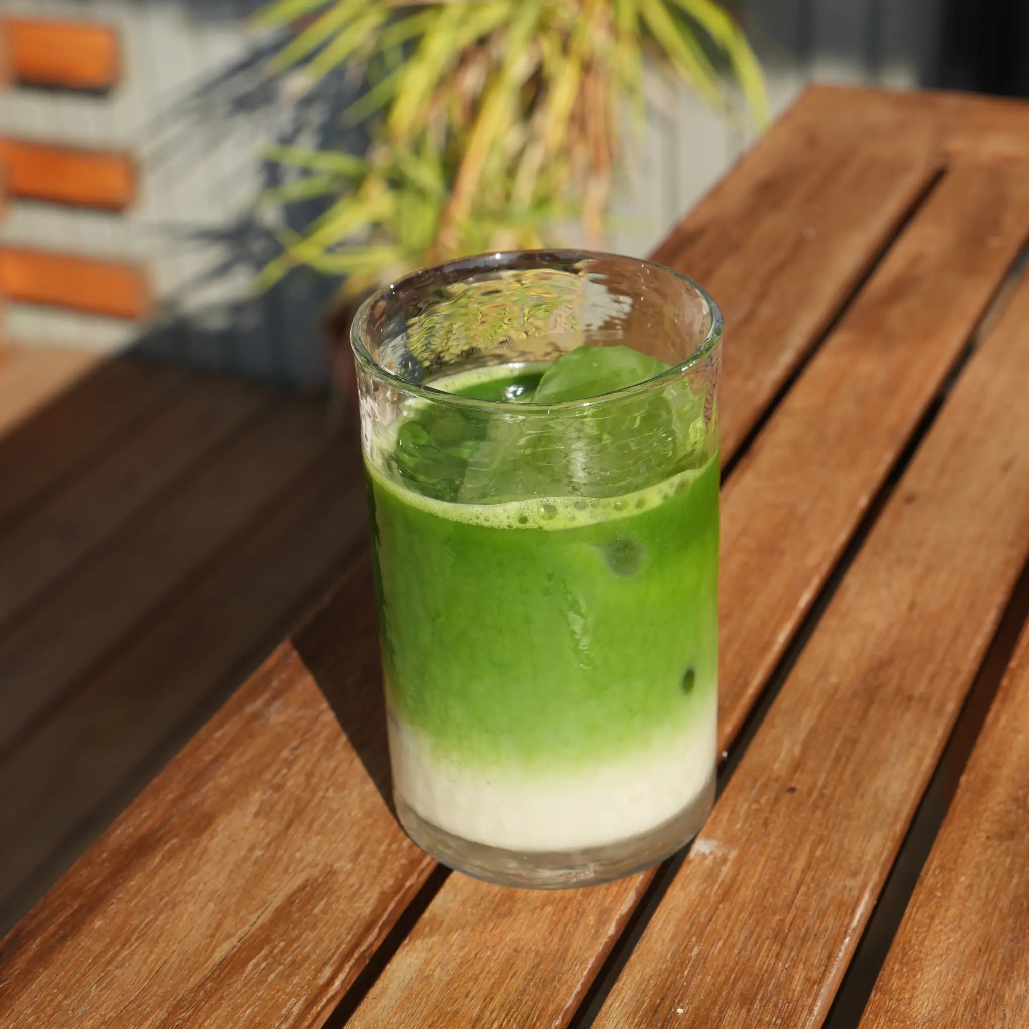 Bebida de Té Matcha Ceremonial Platino con capas de verde y blanco en un vaso sobre una mesa de madera
